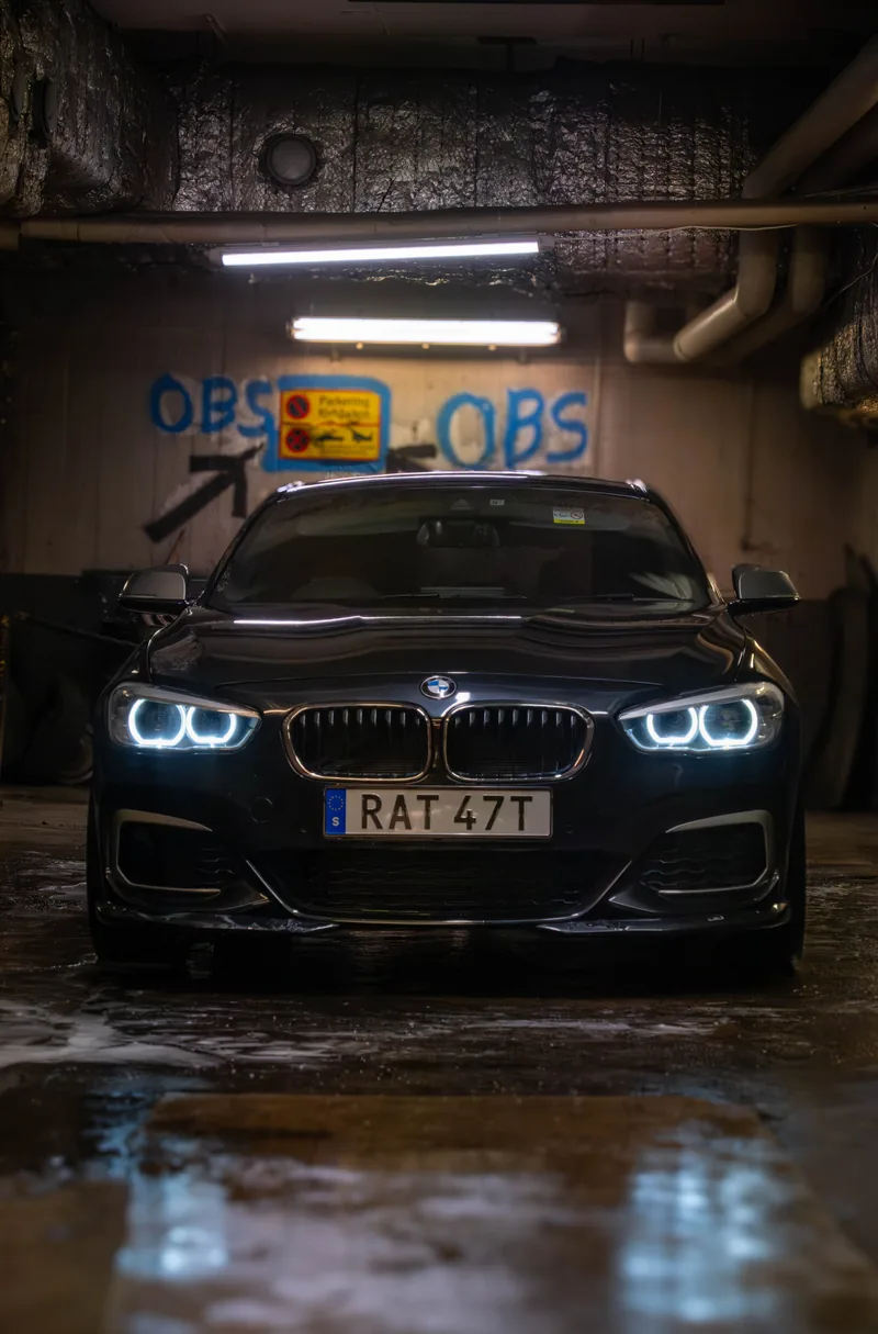 A dark BMW 1 Series shot head-on in an underground garage, headlight rings lit against the concrete.